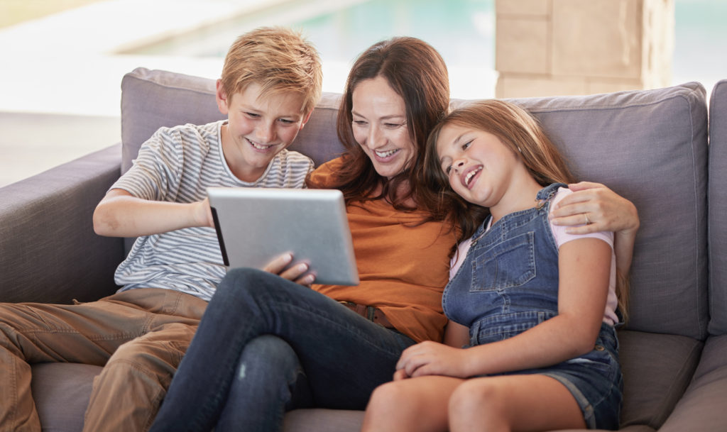 A family of four - parents and two children - gathered around a table, each engaged with a digital device. The parents guide and assist the children, demonstrating how to use the technology effectively. Soft, warm lighting illuminates the scene, creating an atmosphere of learning and collaboration. The children's faces are alight with curiosity and wonder, while the parents wear expressions of patient guidance. In the background, a bookshelf and plants suggest an educational, nurturing environment. The composition is balanced, with the family positioned centrally, emphasizing their collaborative exploration of the digital world.